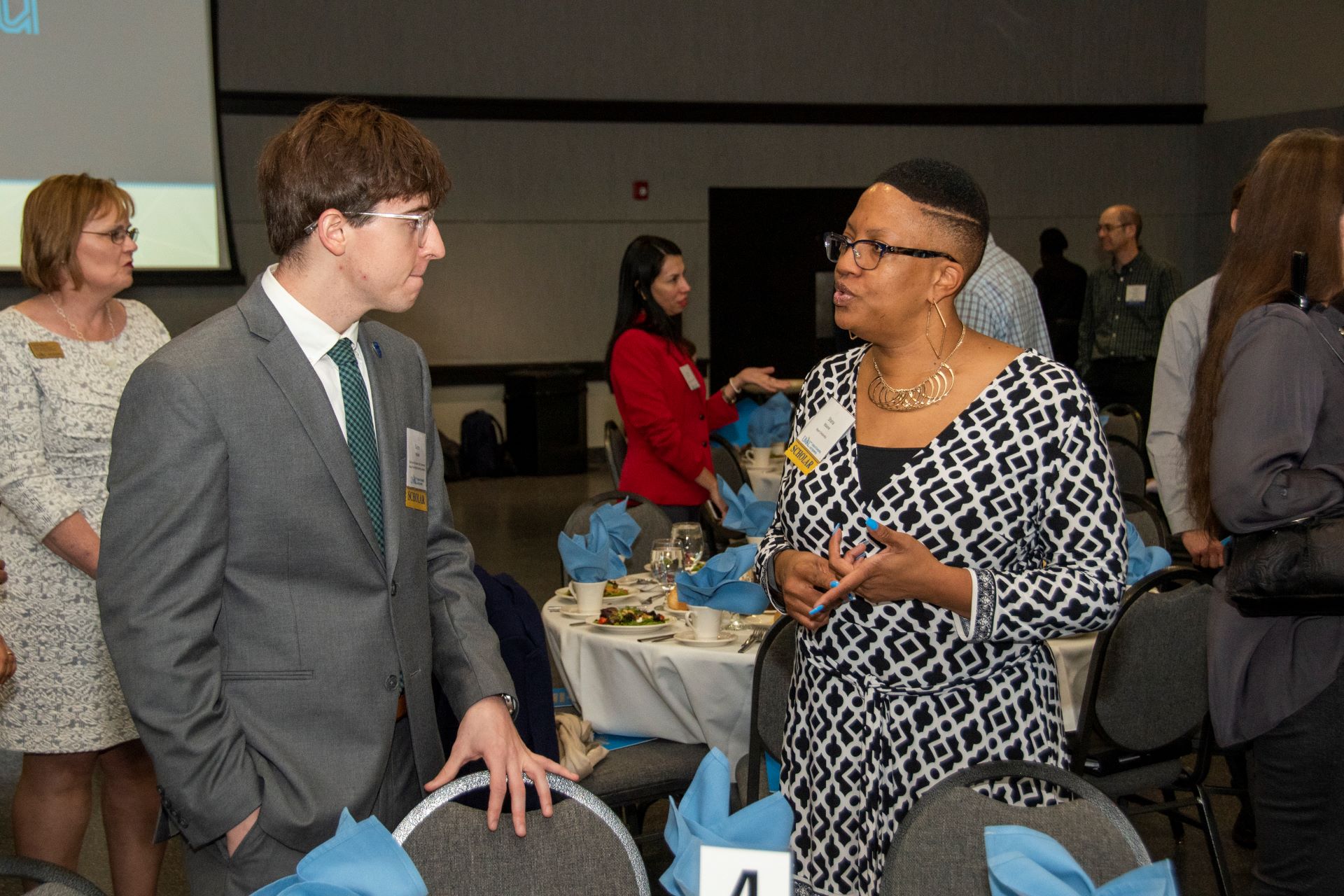 two-scholarship-recipients-speak-to-each-other-standing-by-a-table-at-the-donors-luncheon.jpg